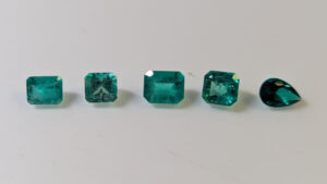5 Emerald stones on a natural surface. One is synthetic.