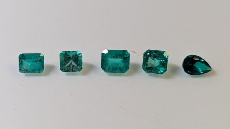5 Emerald stones on a natural surface. One is synthetic.